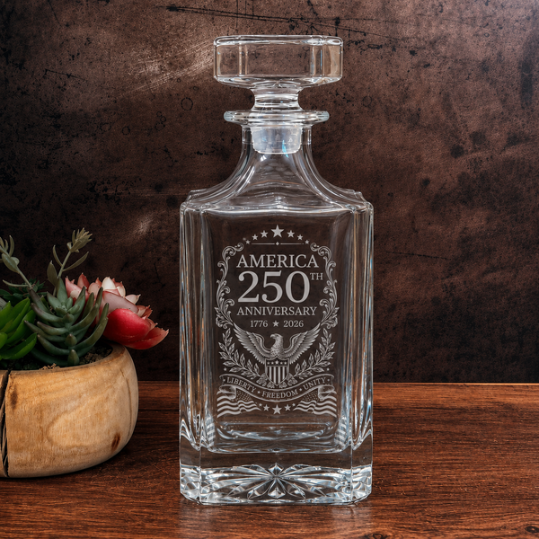 Clear glass decanter with engraved 'America 250th Anniversary' design on a wooden surface.